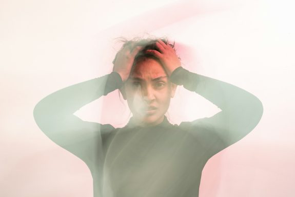 A person with a pained expression holds their head, surrounded by soft, blurred colors.